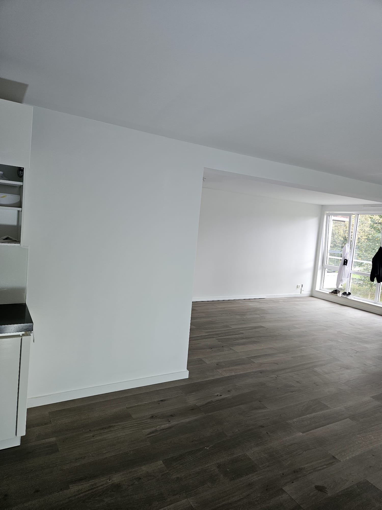 Open woonkamer met keukenblok en gladde witte wanden na stucwerk