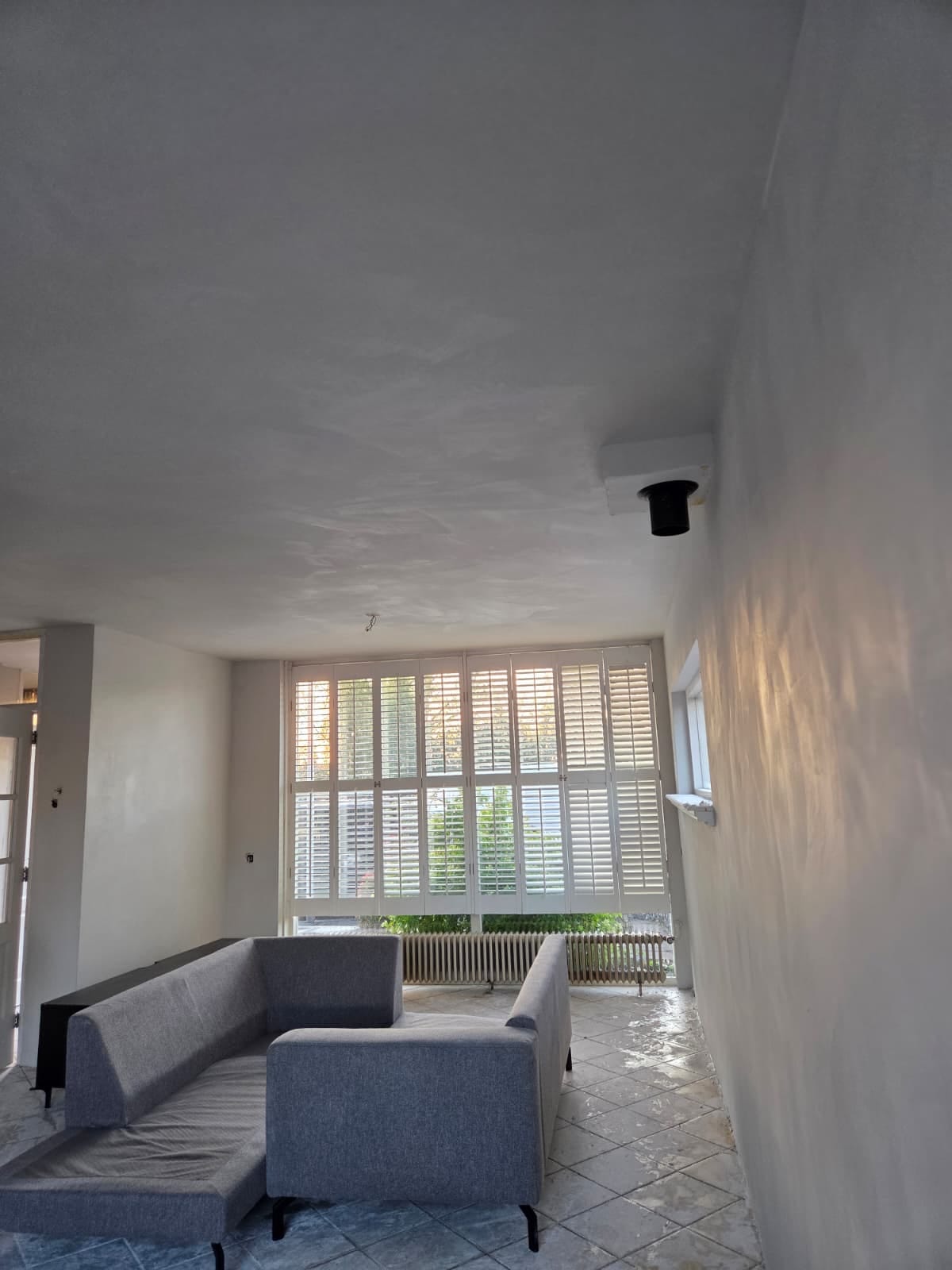 Woonkamer met een gladgestuukt plafond en shutters voor het raam